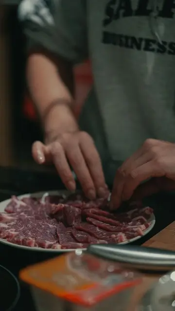 Entertainment placement — Close-up of hands arranging raw meat slices on a plate indoors, dim lighting.